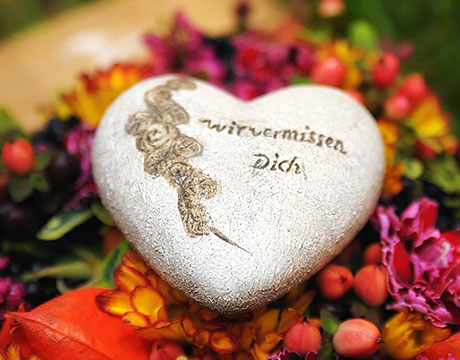 Das Bild zeigt einen herz-förmigen Stein mit der Aufschrift Wir vermissen Dich.